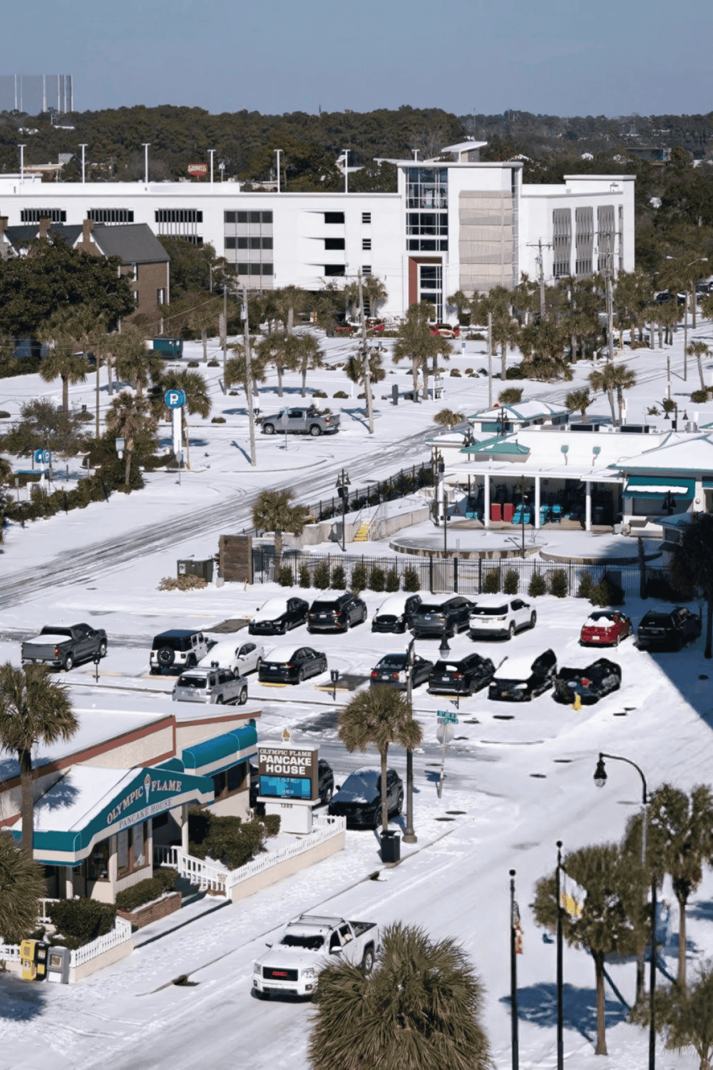 Parking lot and shopping area with snow-covered ground, including Olympic Flame Pancake House.