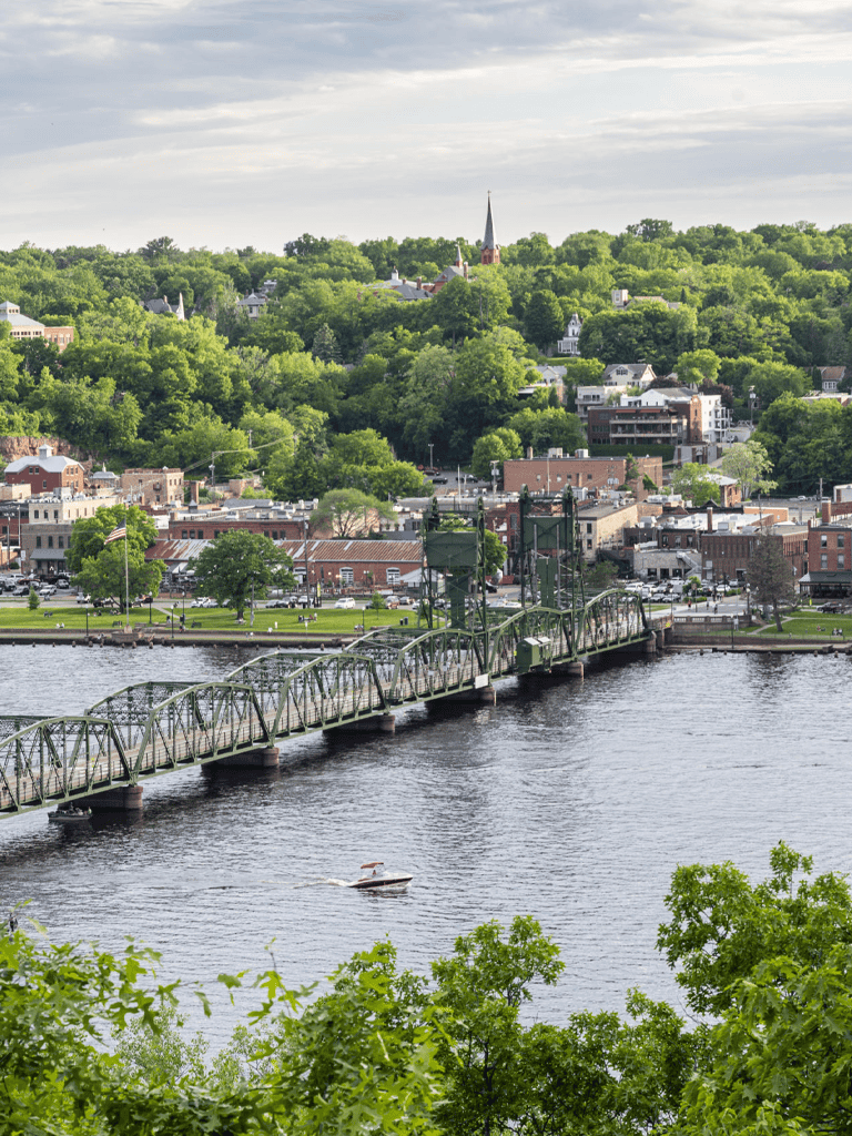 Scenic view of a river with a bridge and lush green hillside town in the background.