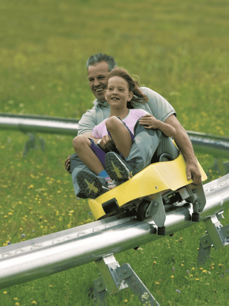 Thrilling amusement park ride with father and daughter enjoying roller coaster adventure outdoors.