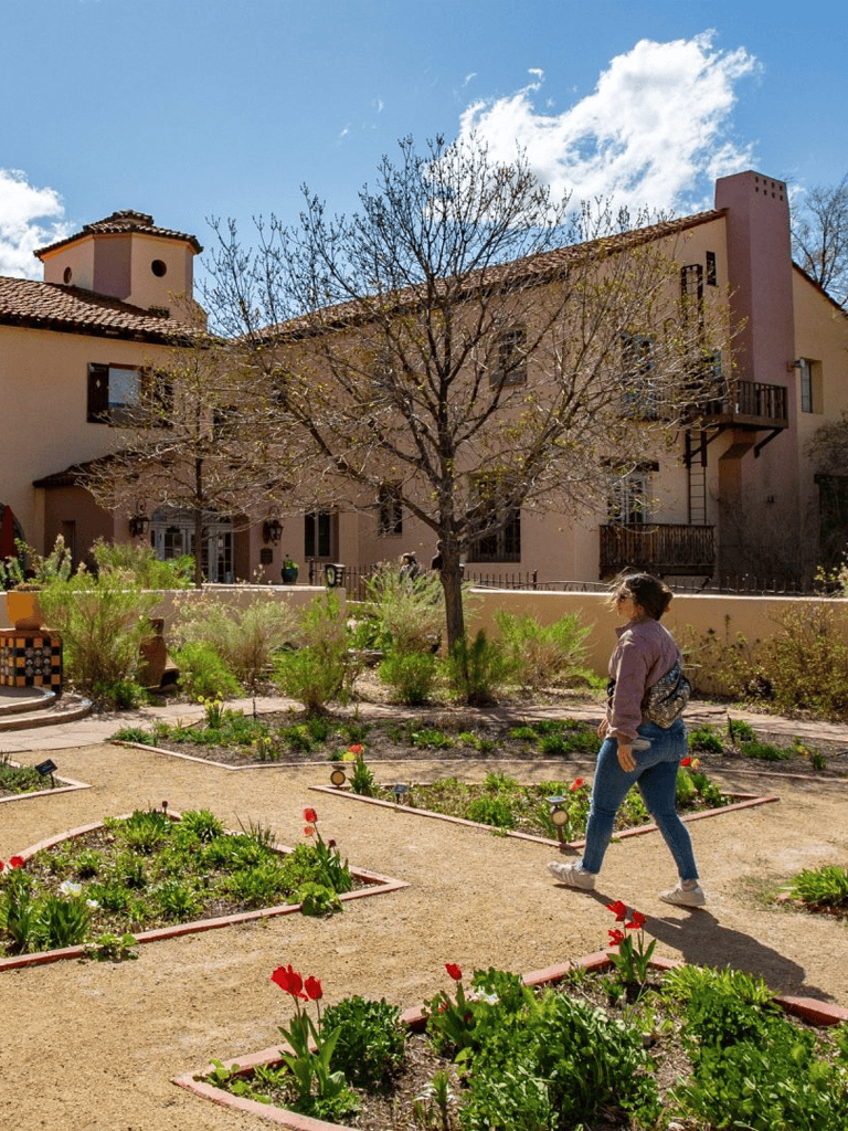 Rooftop garden with city view, woman walking among flowers, scenic outdoor space, peaceful residential area, springtime greenery, QuestForDirections.