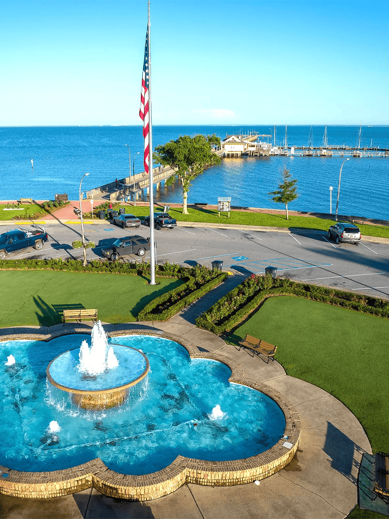 American flag near harbor and water view with fountain and parking lot, scenic coastal scenery.