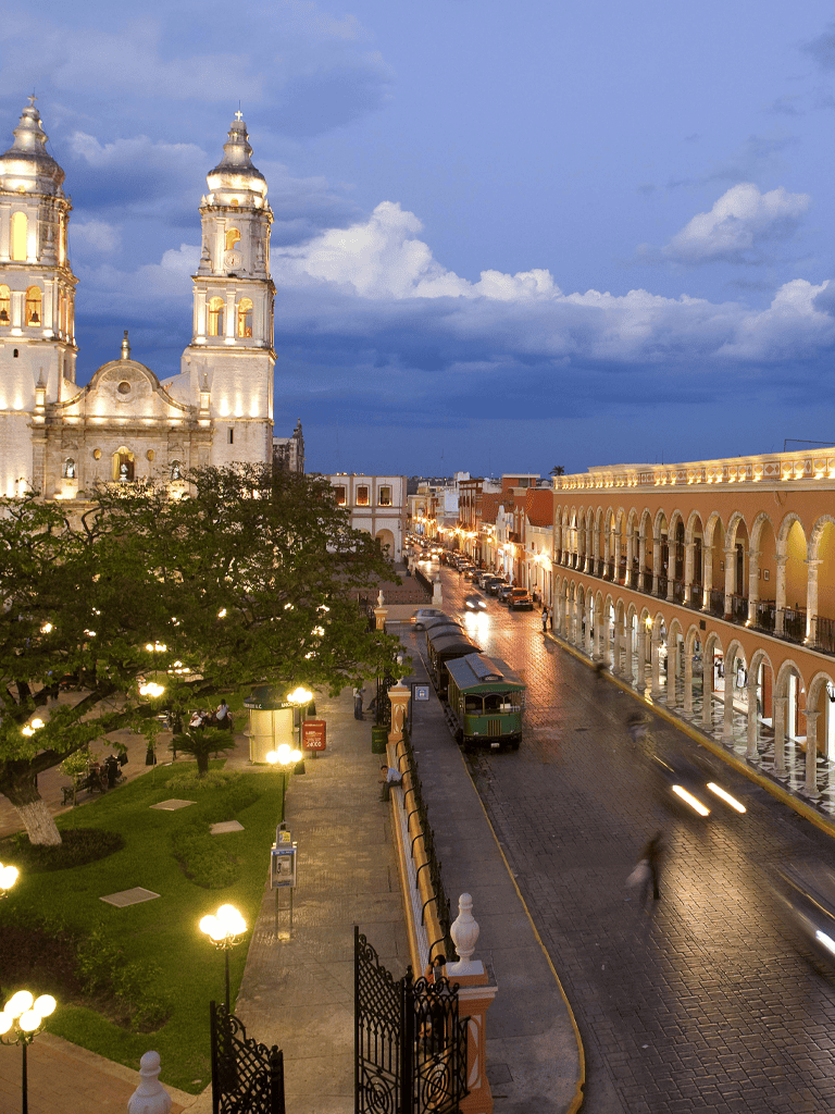 Colorful historic cityscape at dusk with illuminated church and colonial buildings in Mexico.