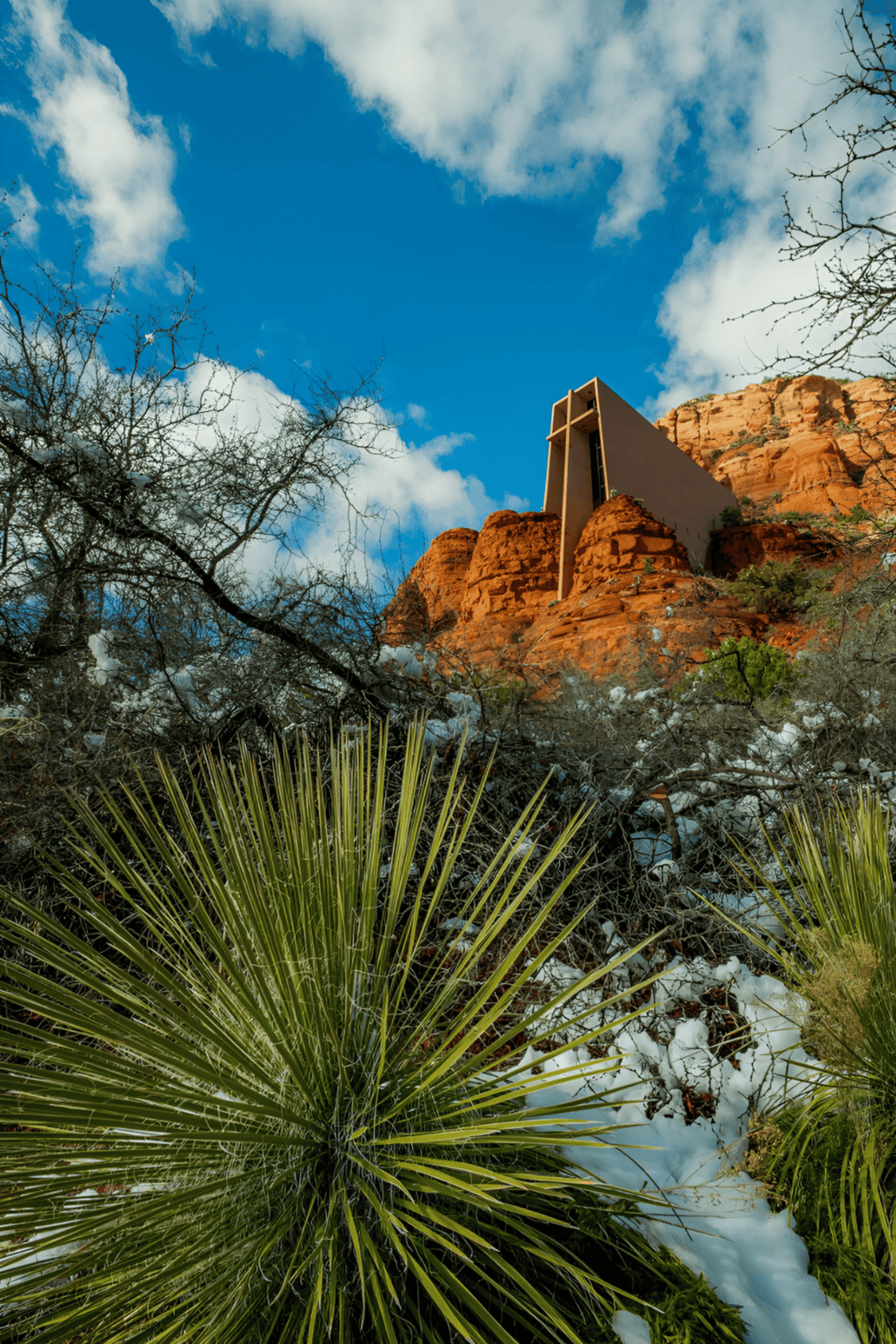 1. Modern house on red rock cliffs in desert landscape with blue sky and clouds.