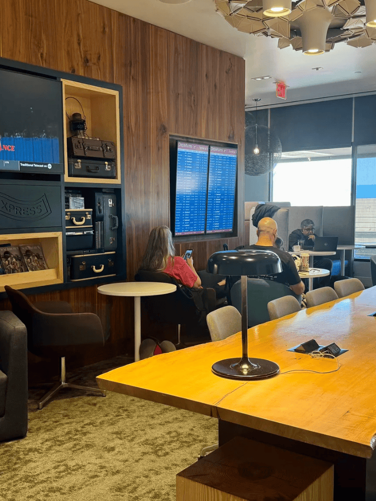 Modern airport lounge with digital flight information displays and travelers using their devices for browsing and communication.