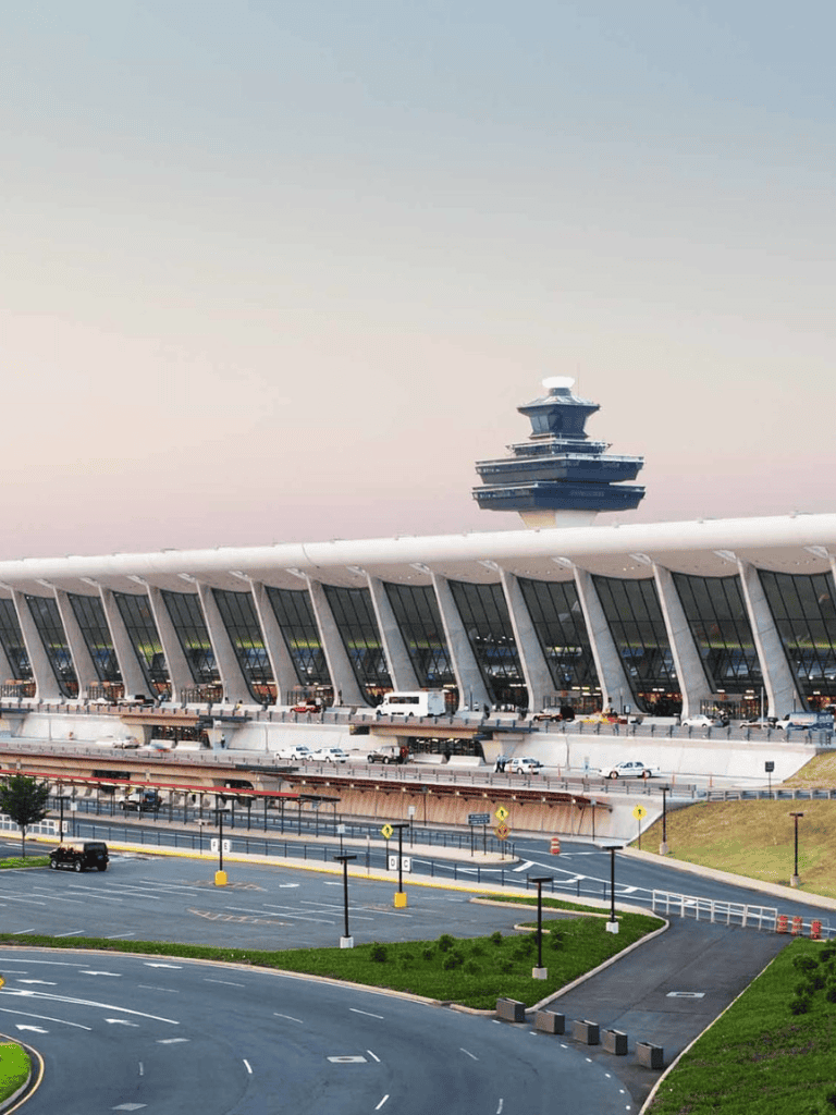 Modern airport terminal with control tower, parking lot, and ongoing vehicle traffic.