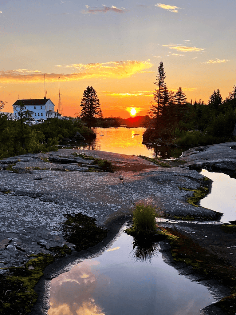Sunset over river with trees and rocky shoreline, scenic natural landscape in Maine.