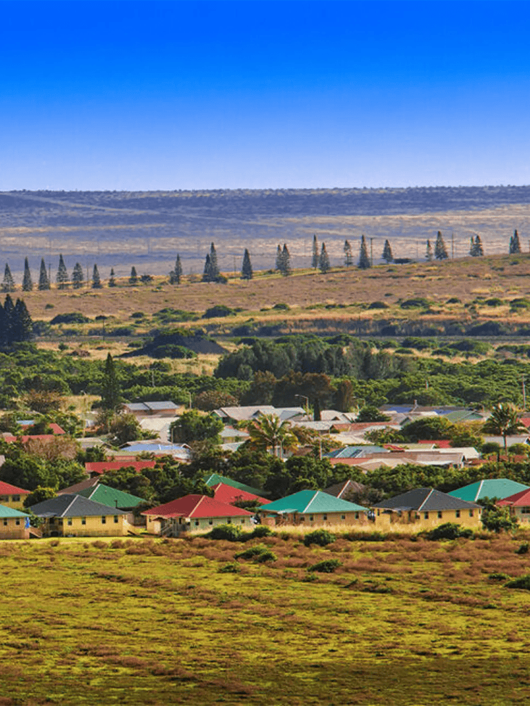 Colorful residential neighborhood with lush greenery and rolling hills in the background.