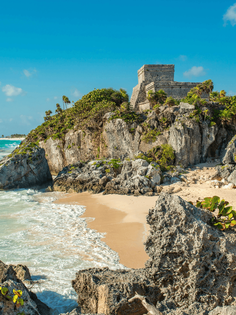 Ancient Mayan ruins on a Caribbean beach, Mexico, with clear turquoise waters and lush greenery.