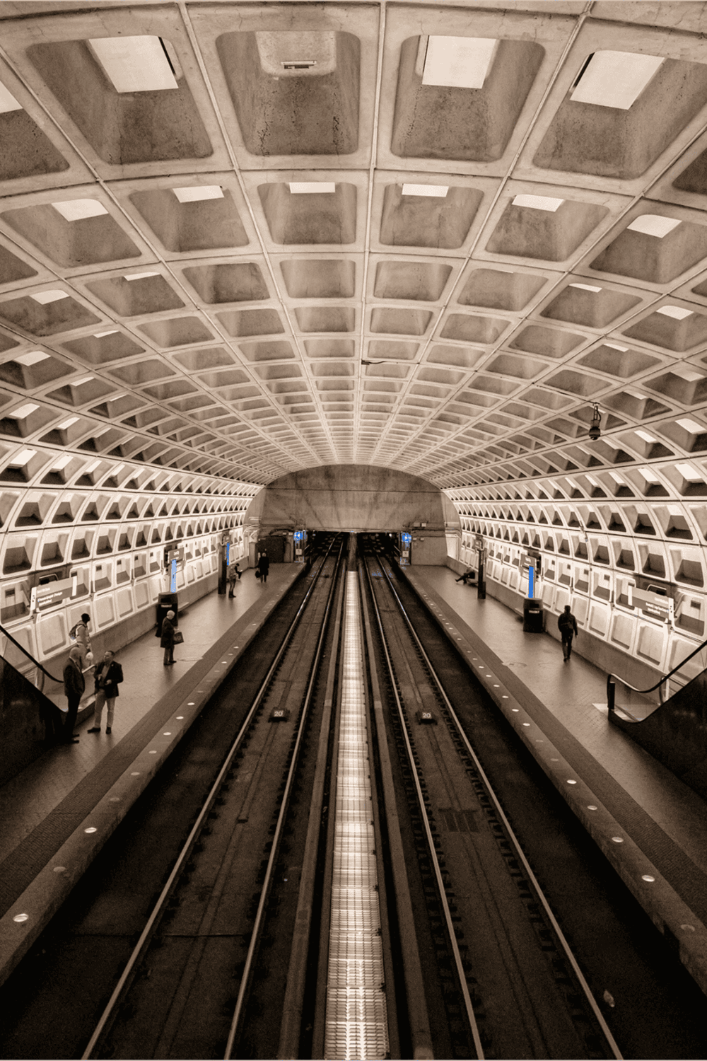 Underground metro station with modern architecture, subway tracks, and passengers awaiting trains.