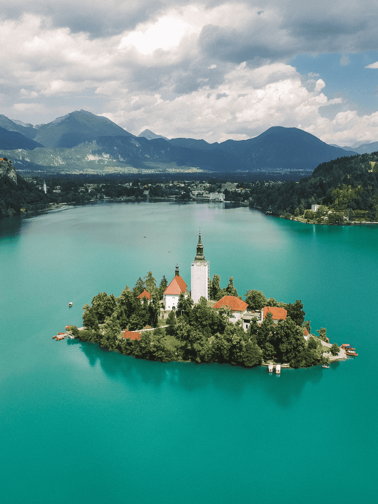 Serene lakeside island with church and mountains in the background, scenic travel destination.