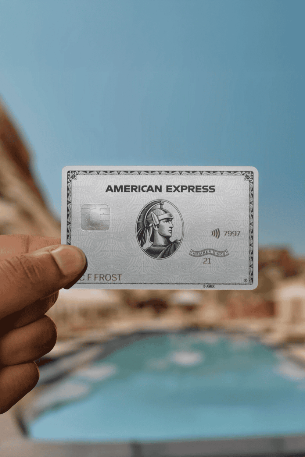 1. American Express credit card held by hand, clear blue sky background.