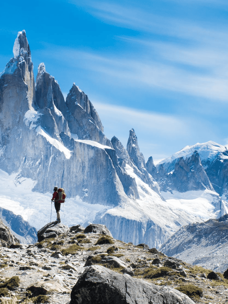 Alpine mountain climber hiking in snow-covered peaks under blue sky.