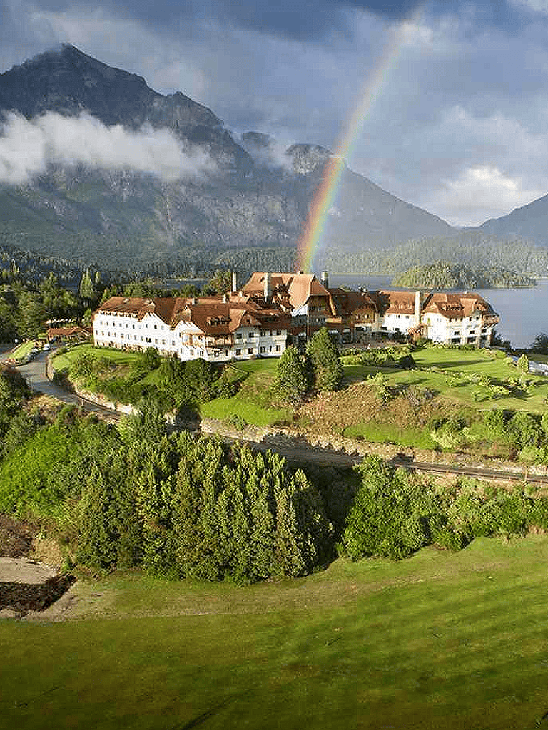 Colorful rainbow over scenic mountain hotel in lush greenery, picturesque destination for travel and exploration.