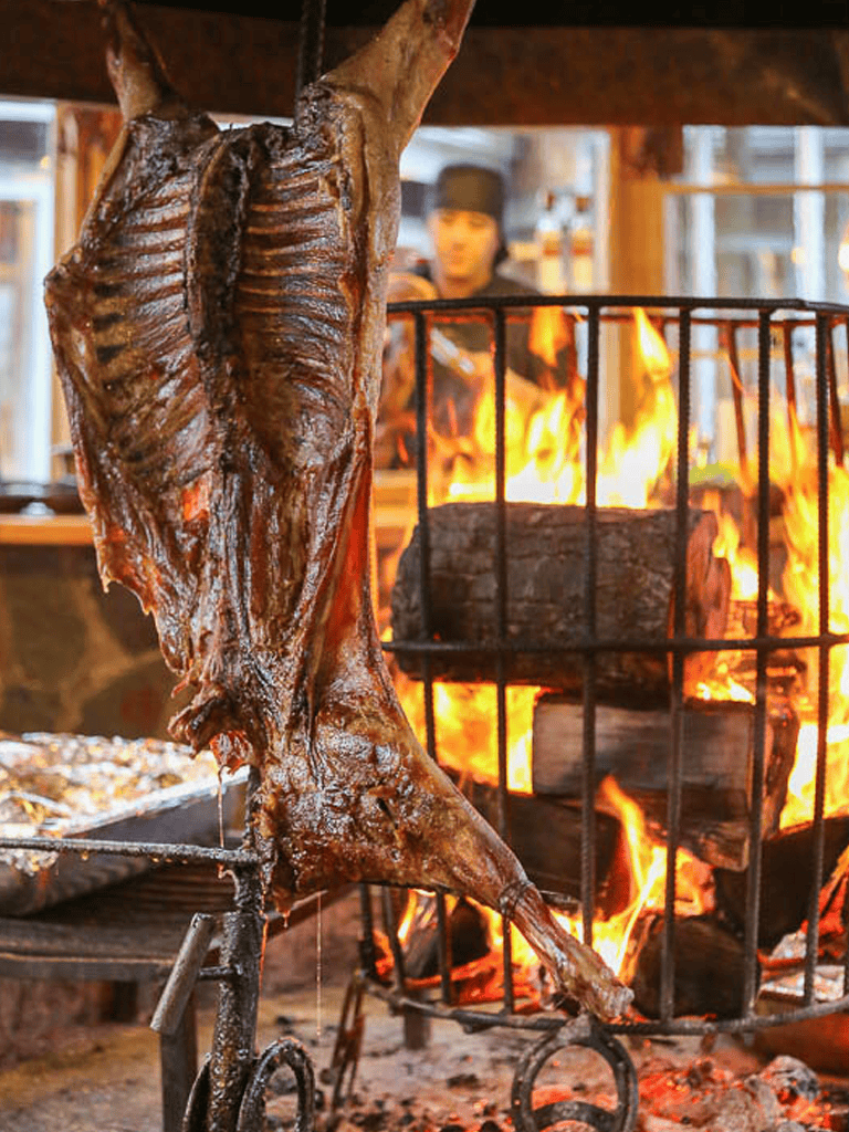 Juicy roasted lamb on a spit over open fire cooking at a rustic restaurant.