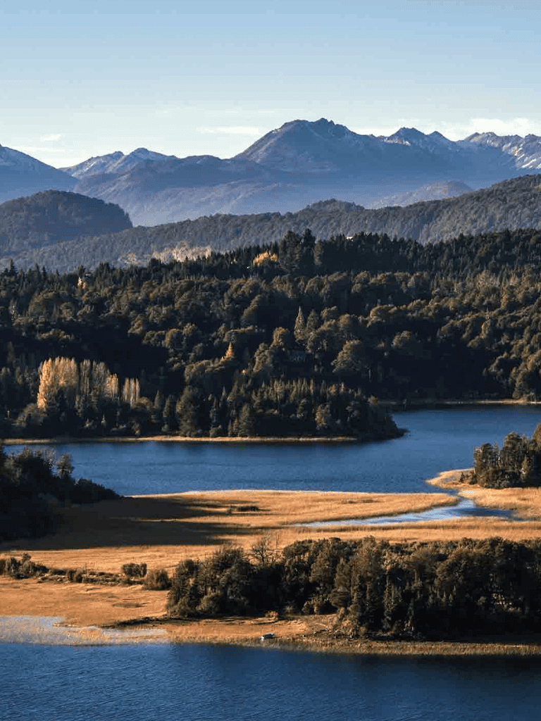 Serene mountain lake surrounded by lush forests and distant snow-capped peaks.