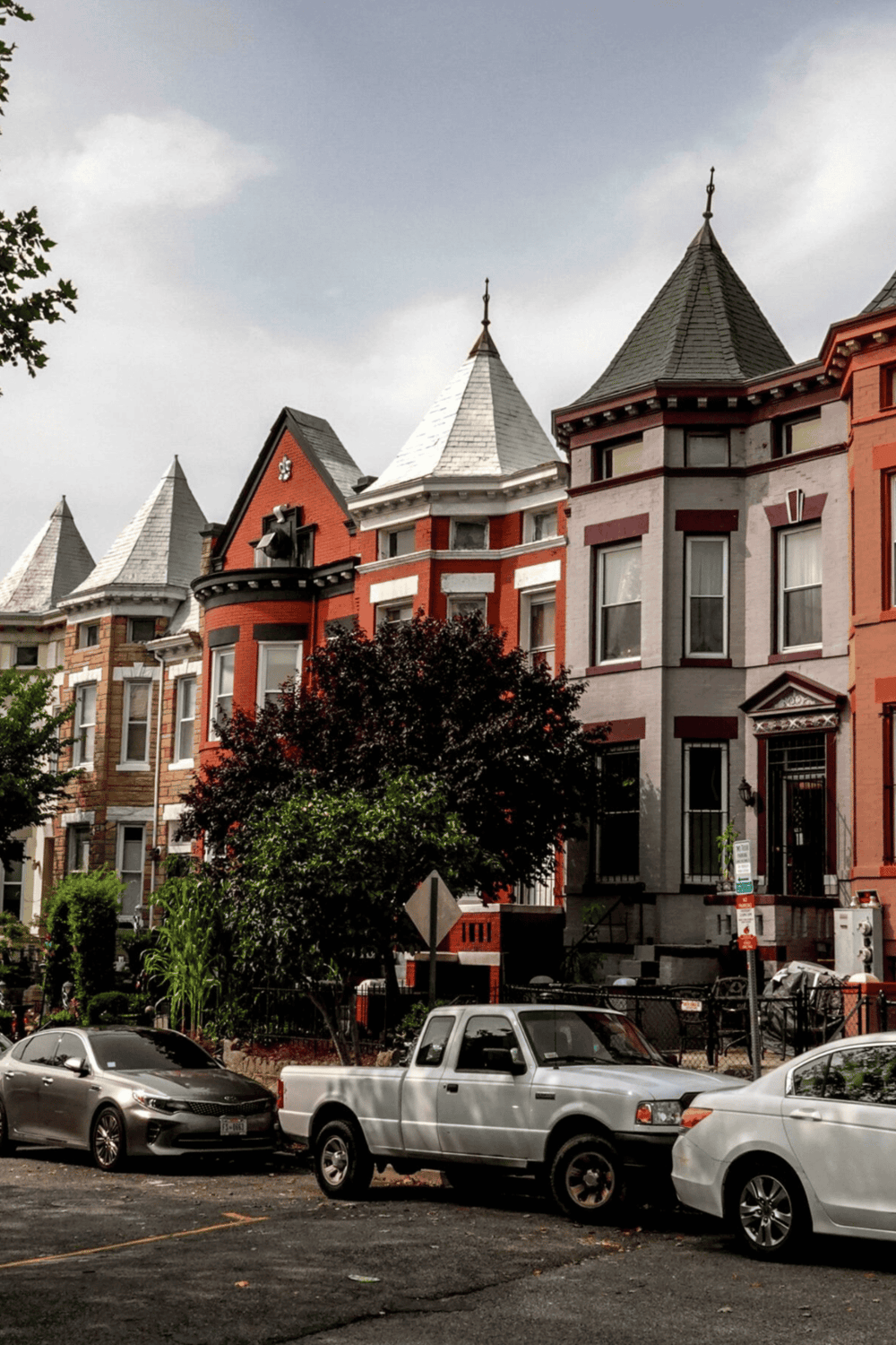 Colorful Victorian-style houses in San Francisco with parked cars and lush trees.