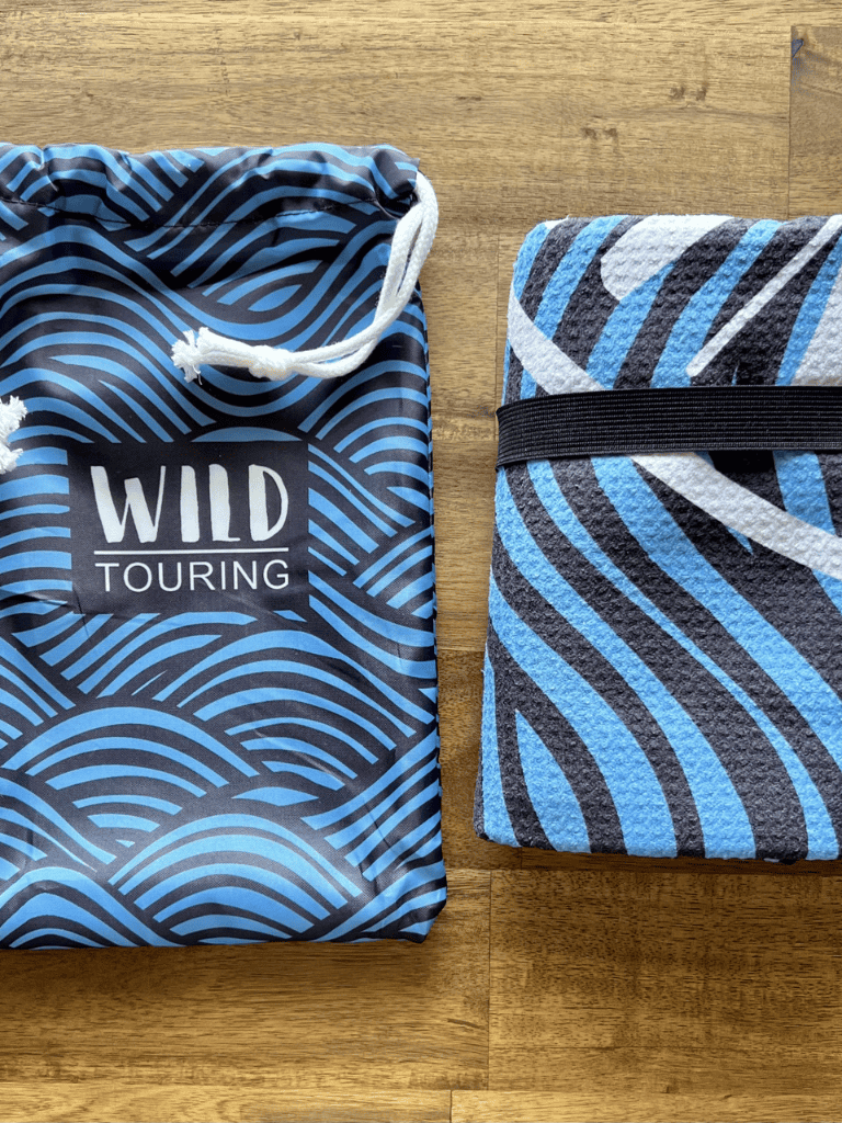 Soft blue and black striped towel with a black strap on a wooden surface for travel and leisure.