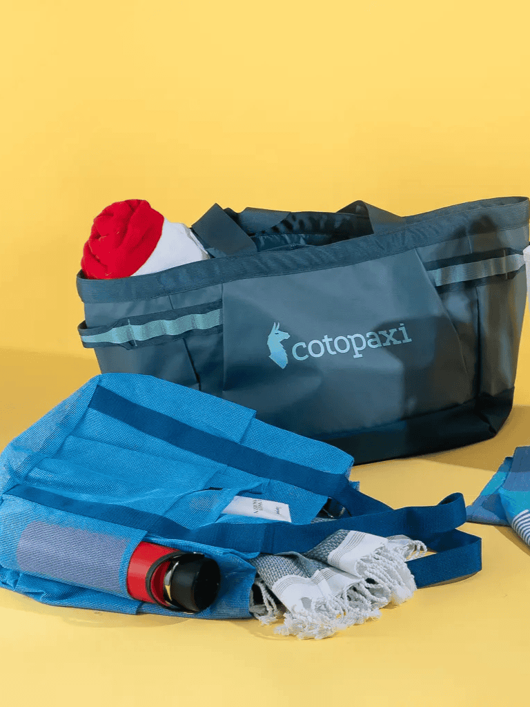 Santa hat in a Cotopaxi travel bag with travel essentials on a yellow background.