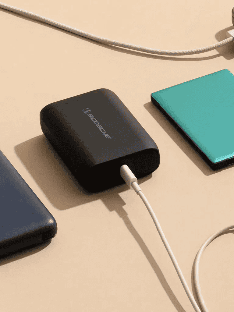 Portable charging device with power bank and smartphones on a beige surface.