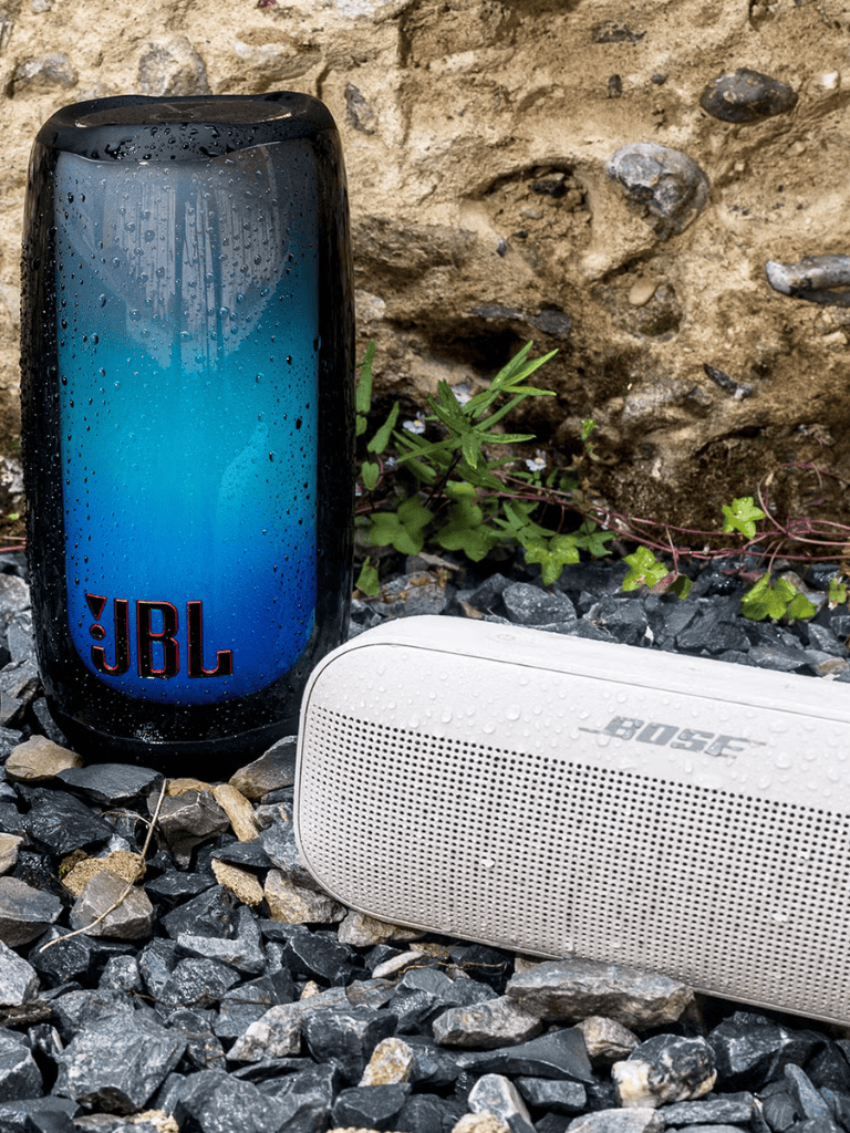 JBL portable waterproof bluetooth speaker outdoors with Bose speaker on rocky ground.