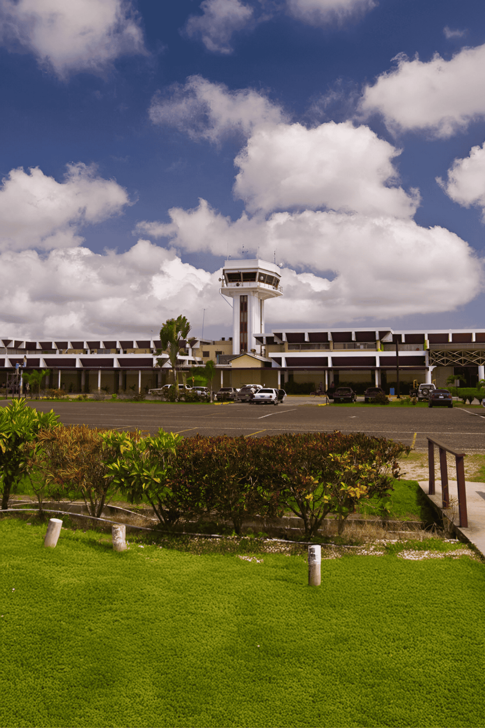 Modern airport control tower at Quest for Directions facility, sunny sky, parking lot, lush greenery.