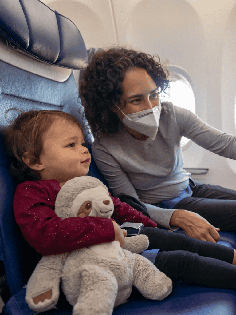 Woman and child wearing masks on airplane seat.