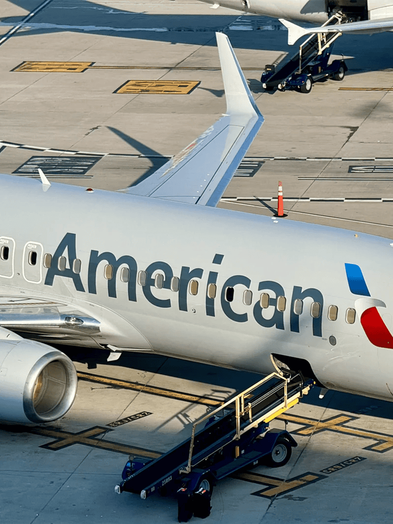 1. American Airlines aircraft on airport tarmac with boarding bridge and ground crew.