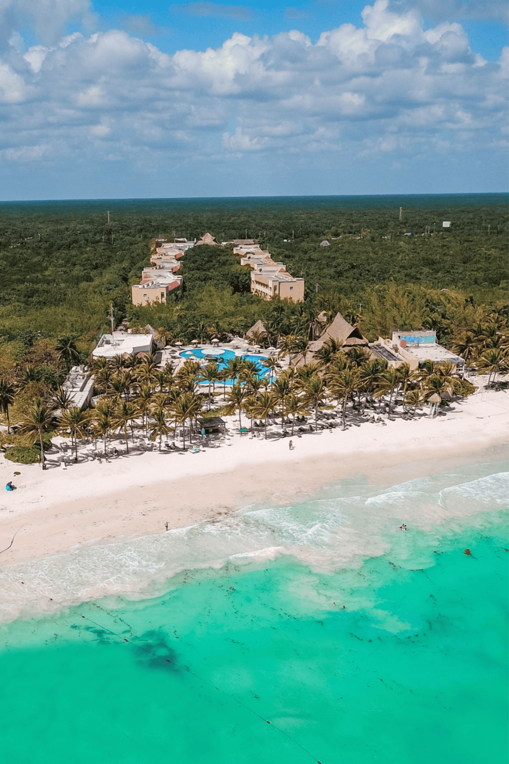 Luxurious beachfront resort with pool, palm trees, and white sand coastline, perfect for tropical vacation.