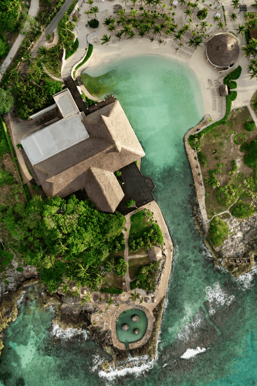 Aerial view of a tropical resort with pool, lush greenery, and ocean waves.