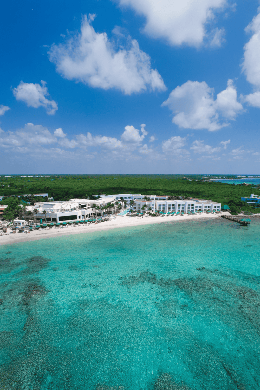 Aerial view of a luxury beach resort with white buildings, turquoise water, and a clear blue sky.