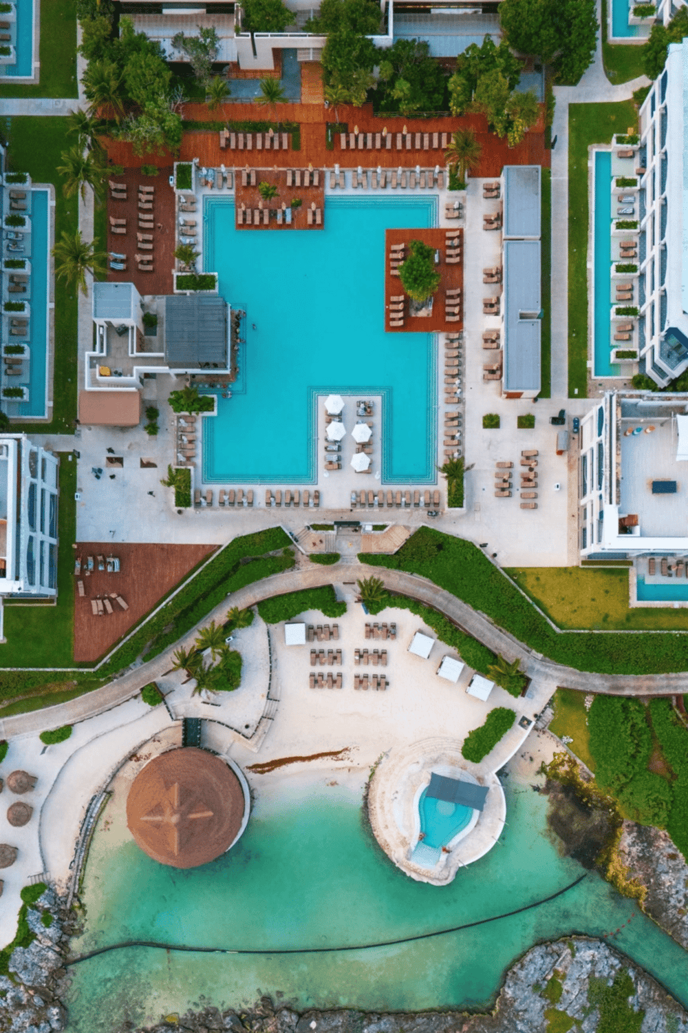 Luxury hotel pool with cabanas, surrounded by modern buildings and lush greenery.