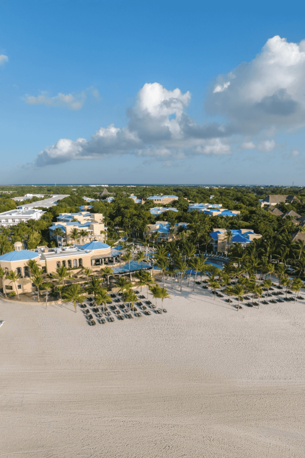 1. Aerial view of luxury beachfront resort with palm trees and blue roofs on sandy beach.