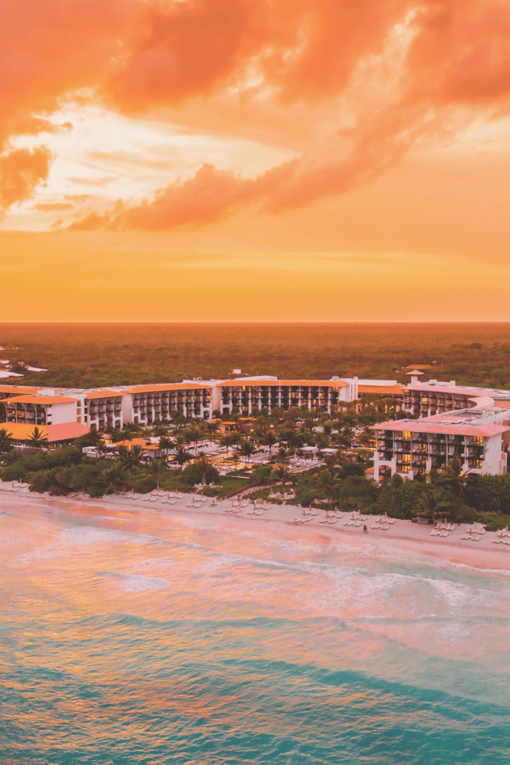 Sunset view of beachfront resort with tropical landscape and ocean, perfect for travel and vacation planning.