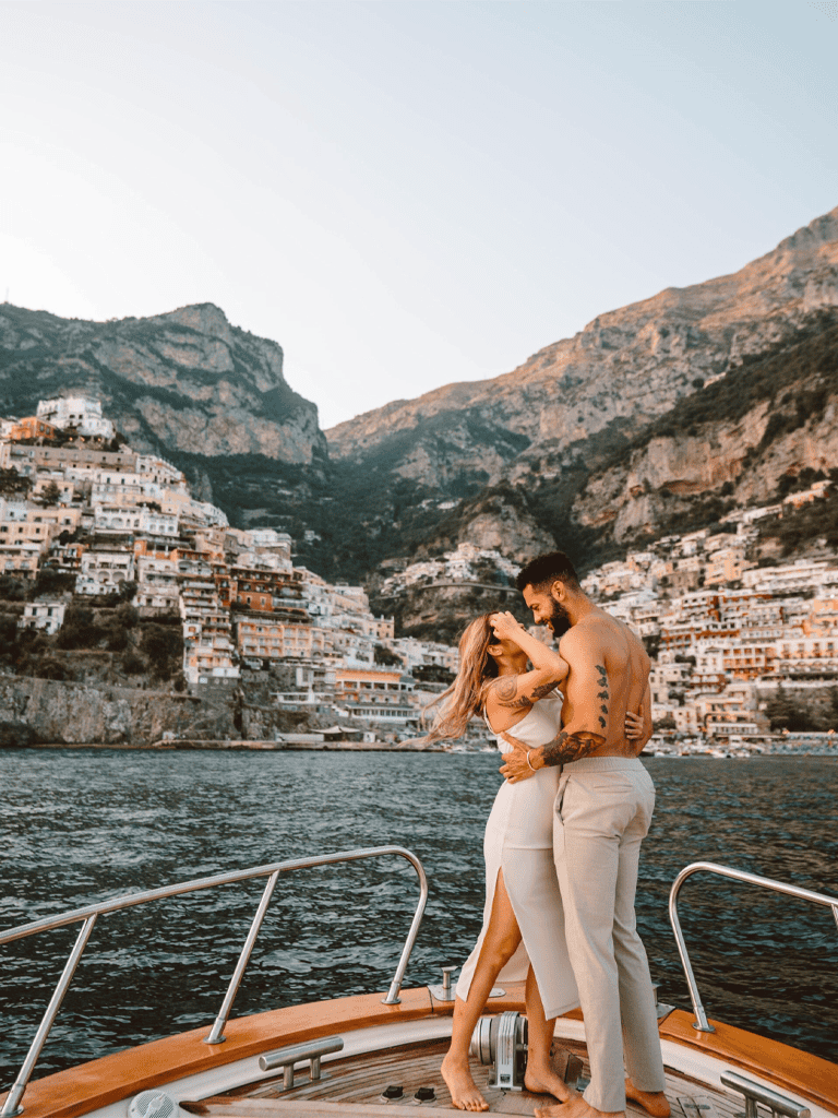 Relaxing couple enjoying romantic moment on yacht with hillside town in Amalfi Coast, Italy.