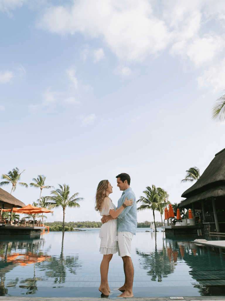 Romantic couple in poolside resort with palm trees and thatched roof bars.