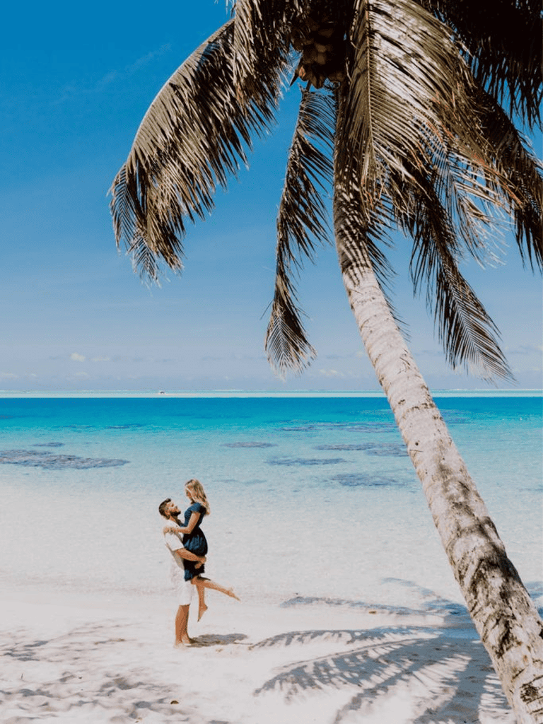 Relaxing beach with palm trees, turquoise water, and a couple enjoying a sunny day by the sea.