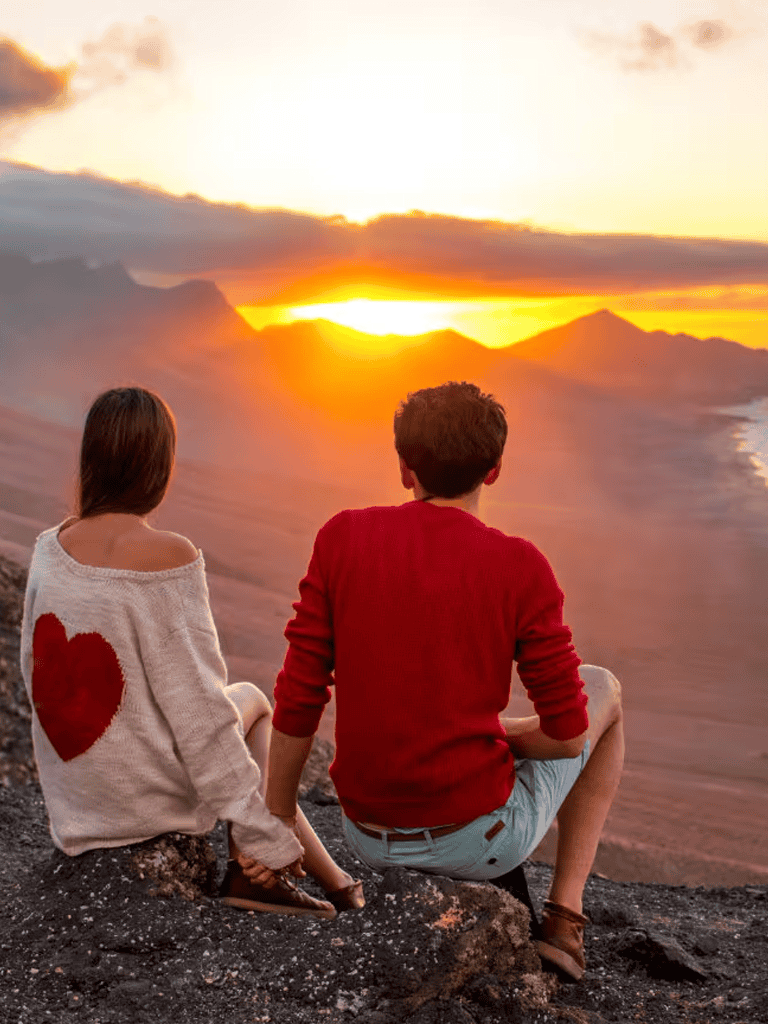 Sunset view with a couple sitting on a cliff overlooking the ocean and mountains, symbolizing travel and adventure with QuestForDirections.