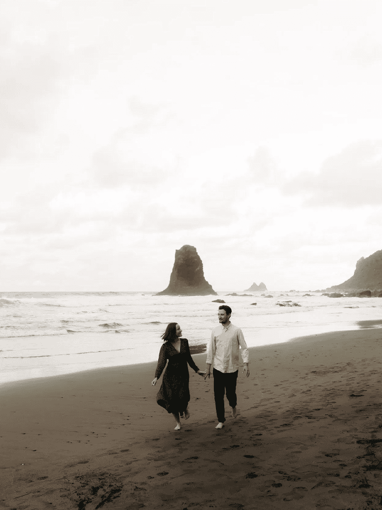 Relaxed couple walking on the beach with sea stacks in the background, romantic coastal scenery, exploring scenic destinations.