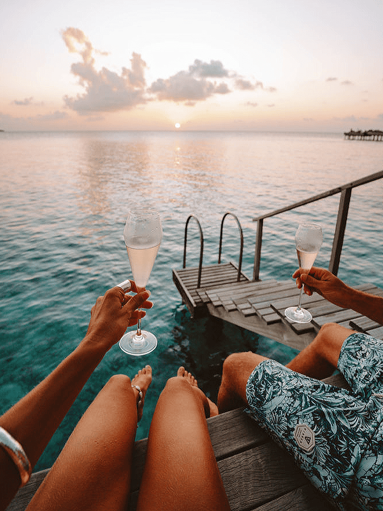 Relaxing ocean view with sunset, two people enjoying champagne on dock, tropical getaway, vacation, paradise.