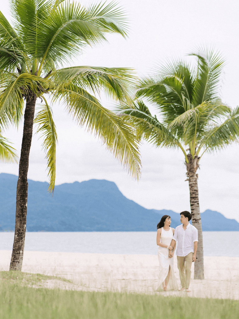 Relaxing couple walking on beach with palm trees and mountains in background, perfect for vacation and travel planning.