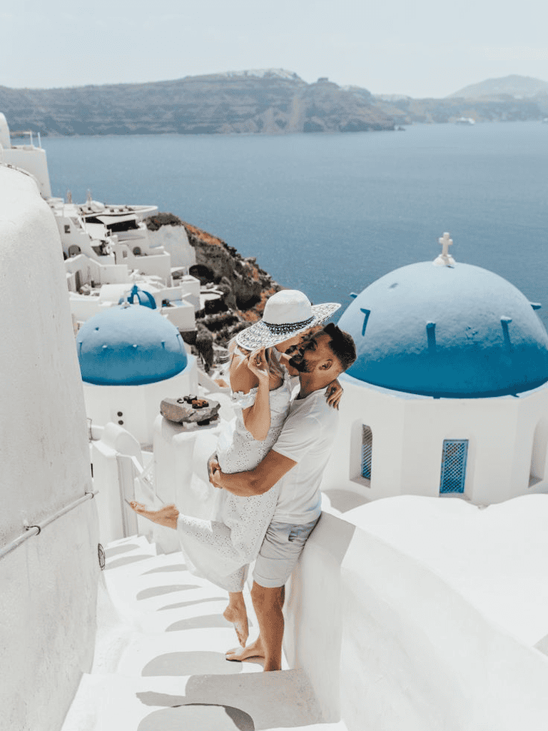 Romantic couple in Santorini with iconic blue-domed churches, vacation scenery, travel destination.