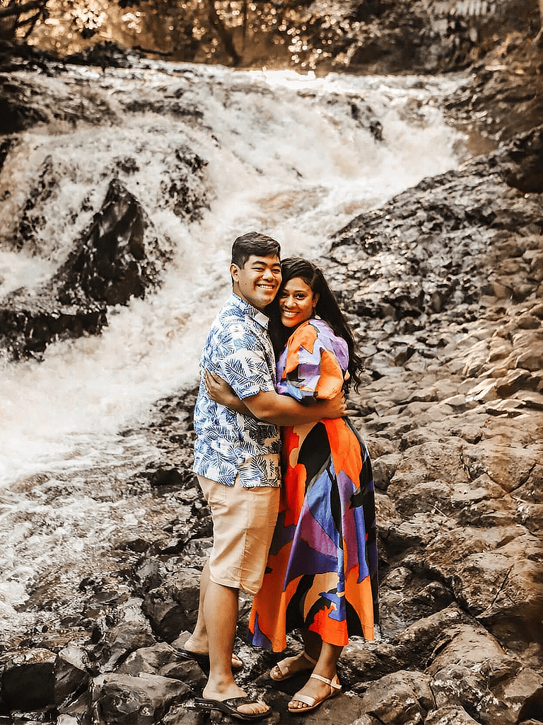 Happy couple embracing by a waterfall in a lush forest setting.
