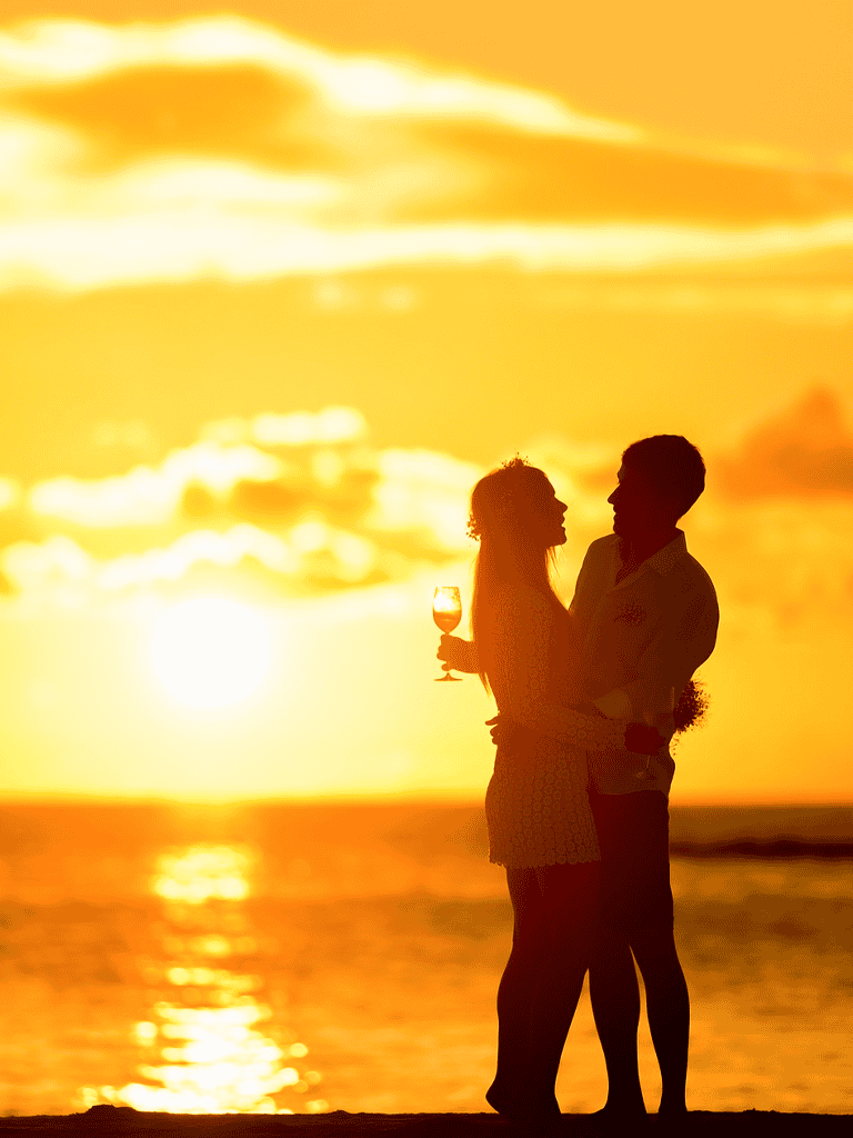 Silhouette of couple with wine glass at sunset on beach for romantic getaway and sunset date ideas.
