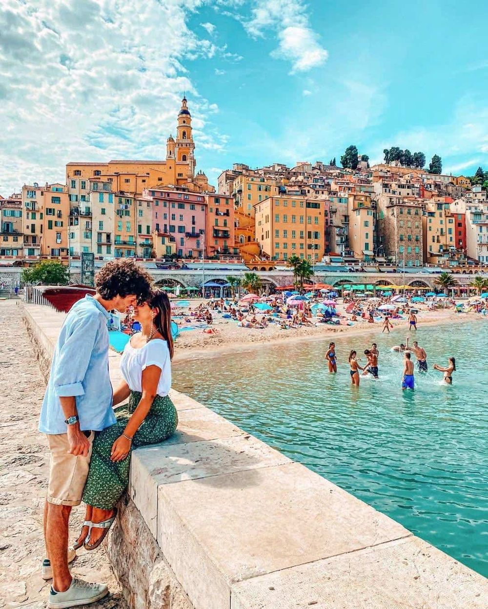 Colorful European coastal city with beach, couple, and sunset sky.