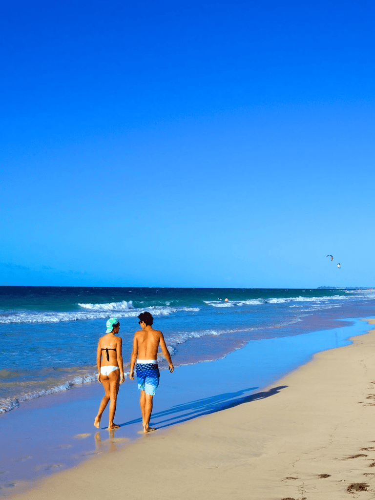 Relaxing beach scene with young couple walking along shoreline, exploring ocean waters and enjoying sunny day.