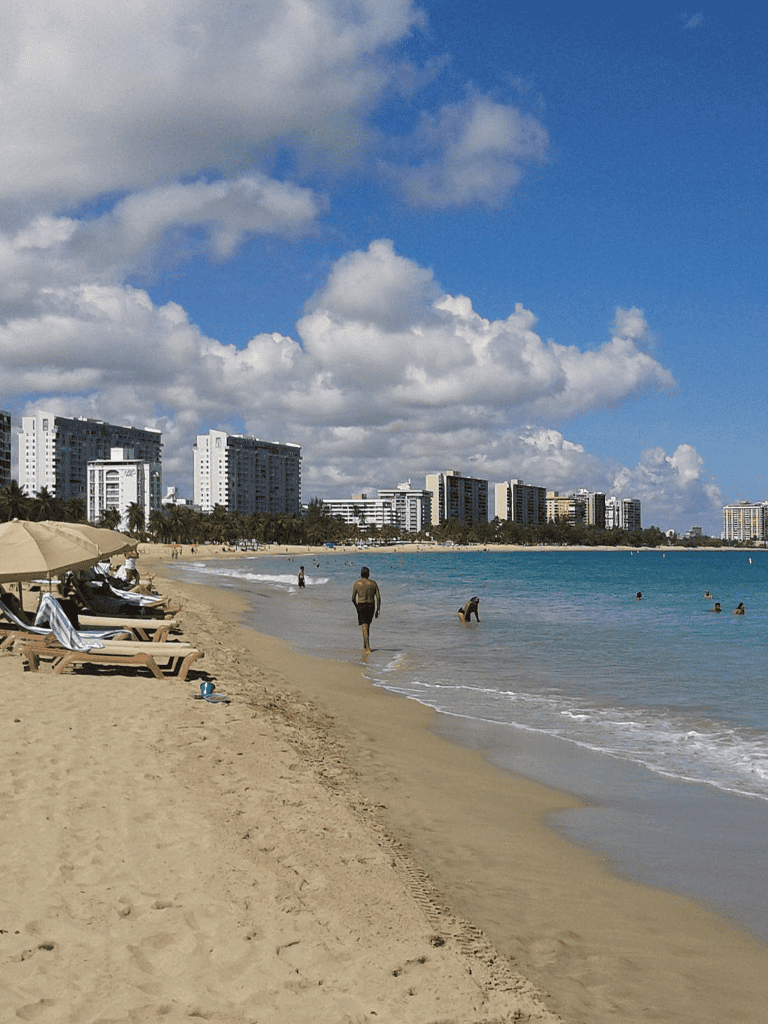 Beach with Lounge Chairs and City Skyline under Blue Sky.