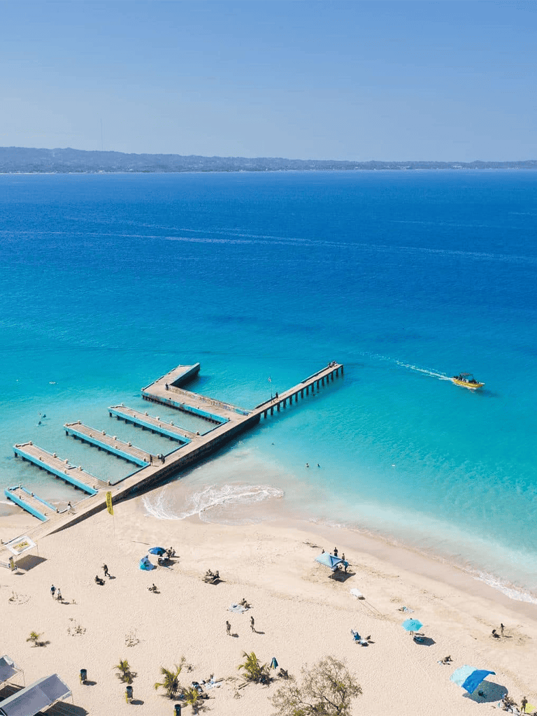 Bright blue ocean with beach and pier, sunny day, people relaxing and enjoying seaside.