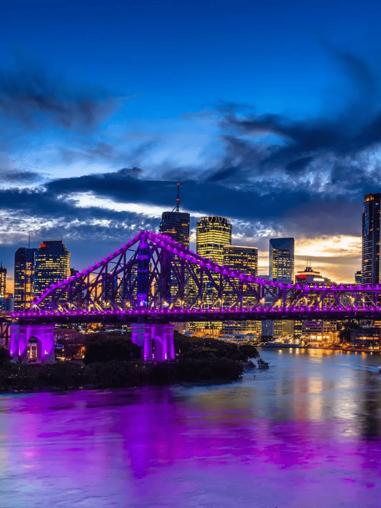 Brightly lit purple bridge over Brisbane River with city skyline at sunset, Queensland Australia, QuestForDirections.