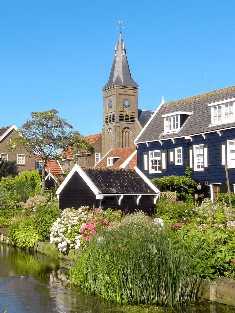 Colorful Dutch-style houses along a water canal with a church steeple in the background, vibrant and picturesque village scene.