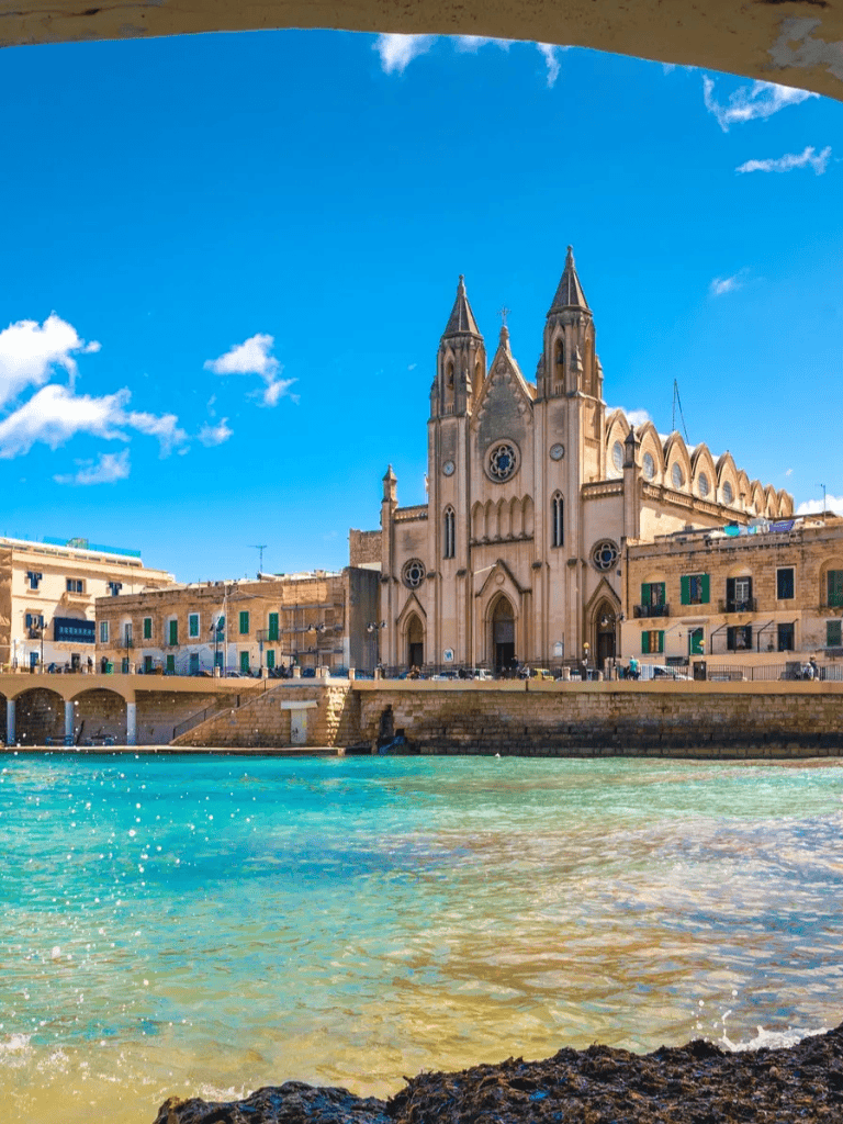 1. Beautiful Maltese waterfront with historic church and vibrant blue sea under sunny sky.